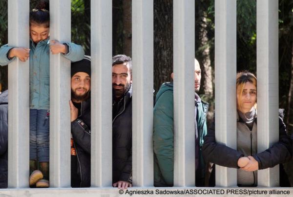 From file: A group of around 30 migrants stands behind a wall built to keep them out in May 2023. According to human rights activists, the group were attempting to seek asylum | Photo: Agnieszka Sadowska / Associated Press / picture alliance